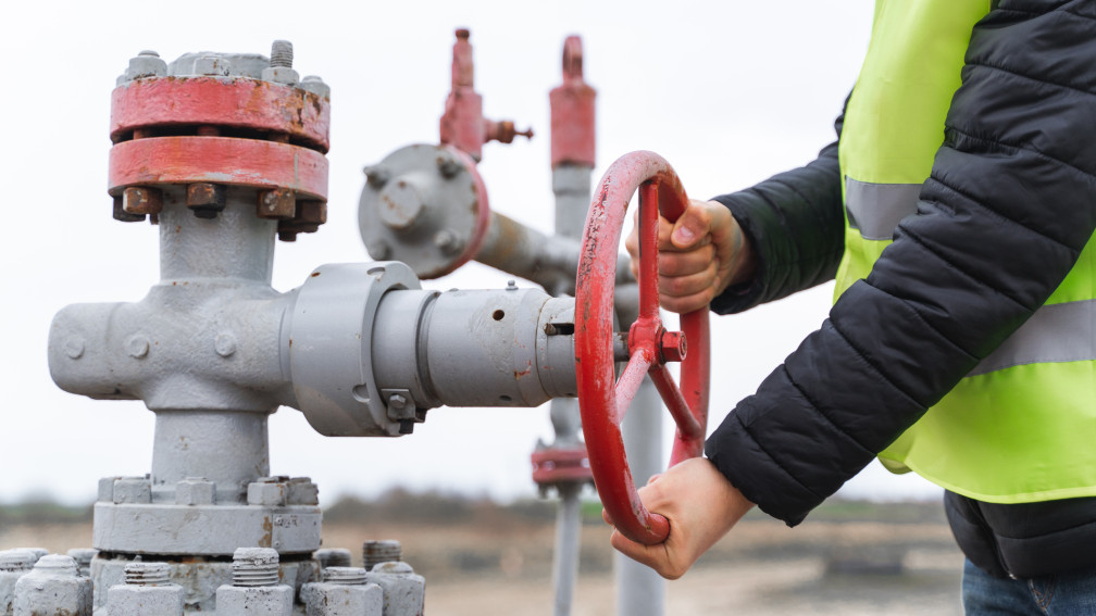 mani di persona con pettorina di sicurezza con catarifrangenti gira la ruota di rubinetto del gas