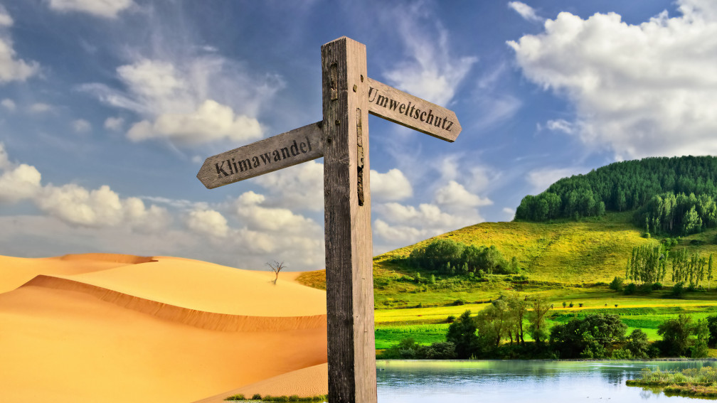 Wegweiser weist auf zwei Landschaften, mit Klimawandel auf eine Wüste, mit Klimaschutz auf eine grüne Landschaft