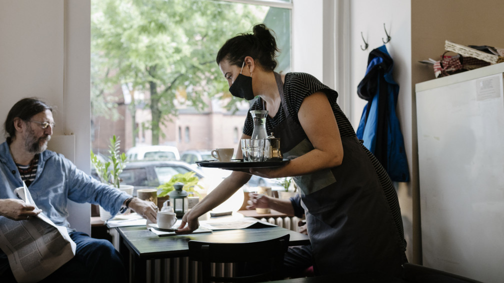 Frau bedient mit Maske einen Mann im Restaurant