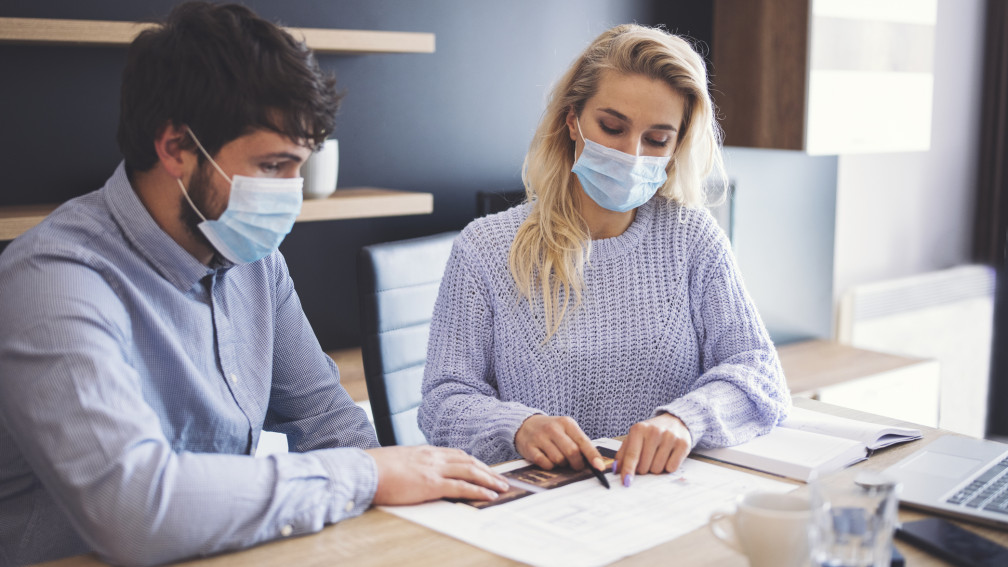 Man and woman work at a desk wearing masks