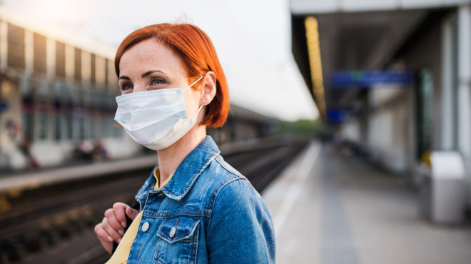 Frau mit Maske steht an Bahnhof