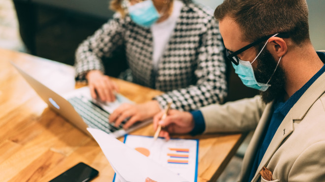 Mann und Frau mit Gesichtsmasken arbeiten am Tisch