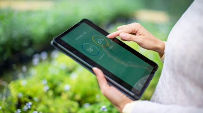 Person hält Tablet über einem Treibhaus