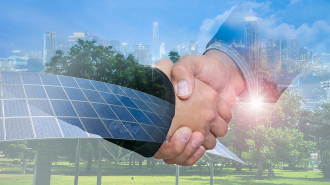 Zwei geben sich die Hand im Hintergrund sind Solarpanels, Windräder