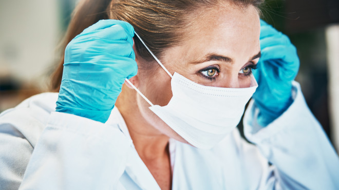 Ärztin mit Schutzhandschuhen zieht Atemschutzmaske an