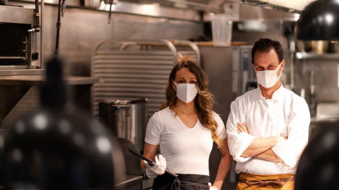 Koch und Köchin mit Gesichtsmasken in der Küche