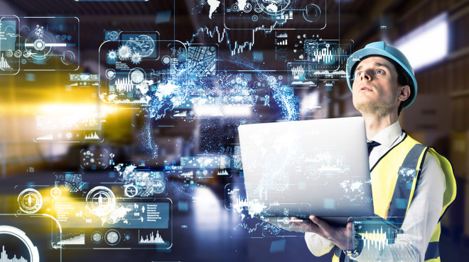 Mann in einem Industriebetrieb mit Laptop und digitaler Projektion vor sich