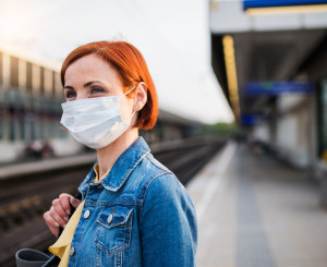 Frau mit Maske steht an Bahnhof