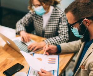Mann und Frau mit Gesichtsmasken arbeiten am Tisch