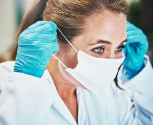 Ärztin mit Schutzhandschuhen zieht Atemschutzmaske an